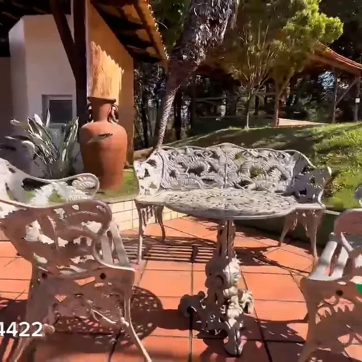 Mesa e cadeiras de ferro no jardim, com gramado ao fundo